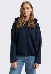 Felpa con cappuccio blu navy, dalla vestibilità comoda, texture a coste, cappuccio con cordino e maniche lunghe, indossata con jeans azzurri chiari.