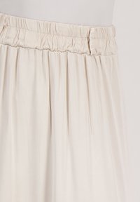 Lichtbeige rok met een elastische tailleband, gemaakt van zacht materiaal en subtiele plooien, die een gladde textuur en vloeiende vorm benadrukt.