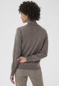 Grauer Rollkragenpullover mit weicher Textur, tailliertem Schnitt und gerippten Bündchen. Getragen mit bedruckten beigen Hosen.