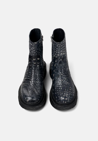 Botas negras hasta el tobillo hechas de cuero texturizado con un patrón de reptil, con una punta redondeada y una cremallera lateral, sobre una suela de goma gruesa.