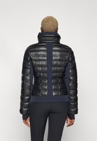 Giacca a vento imbottita con finitura in vernice nera e dettagli in blu navy, colletto alto, pannellatura verticale e polsi a coste; leggera e con texture.