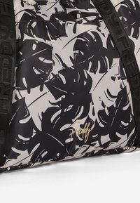 L'immagine mostra una borsa decorata con disegni astratti di foglie in bianco e nero, caratterizzata da un tessuto testurizzato e un logo dorato "Freddy".