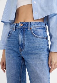 Light blue denim jeans with a high waist, featuring copper hardware, five pockets, and slightly faded areas for a worn effect.