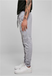 Pantalons de survêtement gris avec poches latérales, taille à cordon, et jambes fuselées. Associés à des baskets blanches. Le tissu semble doux et texturé.