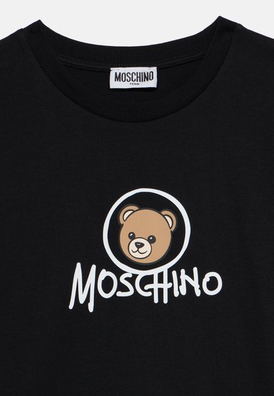 Черна тениска с лице на плюшено мече вътре в кръг и думата Moschino отпечатана отдолу с бели букви.