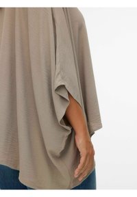Løs pasform taupe bluse med brede ærmer, tekstureret stof og et svævende design. Hånd synlig mod det glatte materiale.
