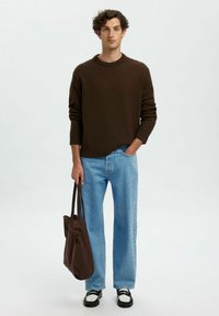 Brūns adīts krekla svārks ar apaļu kakla izgriezumu, gaišzilas taisnas kājas džinsi, melni un balti apavi, tur brūnu somu. Minimālistisks dizains, gluda tekstūra.