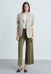 Blazer oversize gris clair, haut crème, pantalon large olive et ceinture marron. Talons aiguilles marron, tissu lisse et design structuré.