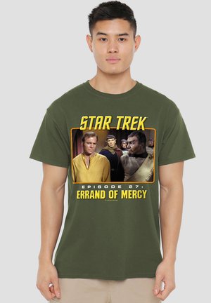 Young man wearing olive-green Star Trek t-shirt featuring characters from episode 27, "Errand of Mercy," in yellow and black text with image panel.