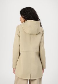 Giacca impermeabile beige con cappuccio, dotata di taglio dritto, maniche lunghe e un'apertura sul retro per maggiore comfort e libertà di movimento.