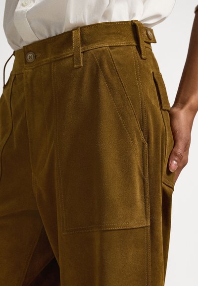 Pantalone od smeđeg antilopa visokog struka s prednjim džepovima, okomitim šavovima i velikim bočnim džepovima. Teksturirani materijal s mekanim završetkom.