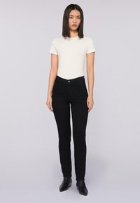 Jeans ajustados negros con una textura suave y diseño de cinco bolsillos, combinados con una camiseta de manga corta gris claro y botas negras hasta el tobillo.