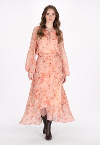 Langes, fließendes Kleid aus transparenter Koralle mit floralem Druck. Verfügt über einen Bindekragen, lange Ärmel und einen asymmetrischen Saum. Getragen mit dunklen Knöchelstiefeln.