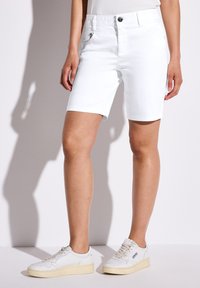 Pantalones cortos de mezclilla blanca con dobladillos enrollados, con bolsillos delanteros y traseros. Combinados con zapatillas blancas y una blusa ajustada. Textura suave.