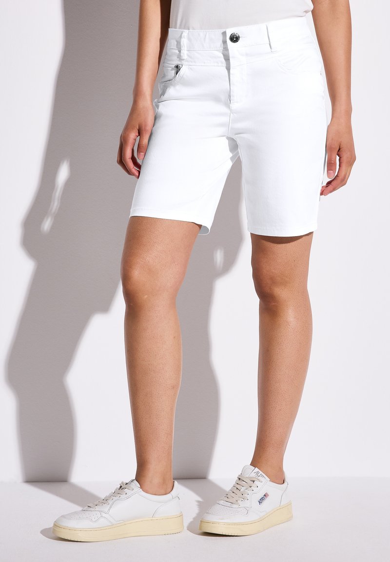 Pantalones cortos de mezclilla blanca con dobladillos enrollados, con bolsillos delanteros y traseros. Combinados con zapatillas blancas y una blusa ajustada. Textura suave.