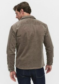Brown corduroy jacket with a collar, featuring vertical ridges and buttoned cuffs, displayed from a back view. Denim jeans visible below.