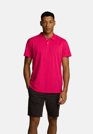 Jasnoróżowa koszulka polo z klasycznym kołnierzykiem, krótkimi rękawami i dopasowanym krojem. Połączona z ciemnymi szortami, co podkreśla swobodny styl.