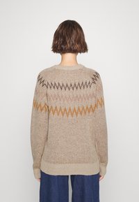 Jasno beżowy sweter dzianinowy z wzorem w zygzaki w odcieniach brązu, różu i pomarańczy. Posiada okrągły dekolt oraz ściągacze przy mankietach i u dołu.