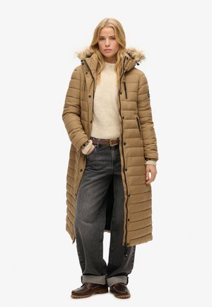 Lange, gevoerde jas in tan met een met bont gevoerde capuchon, rits- en drukknoopsluiting, zijzakken, gecombineerd met een lichte trui en losse donkere jeans.