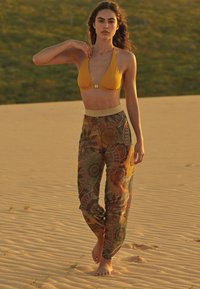 Bikini amarillo con cuello halter y detalle de cierre, combinado con pantalones estampados en tonos tierra, que presentan diseños circulares y una cinturilla suave.