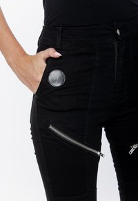Czarne, dopasowane dżinsy z panelem, z boczną kieszenią na zamek i brandowym metką z przodu. Gładka tekstura i solidny materiał.