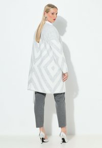 Lange grijs en wit gestreepte jas met diagonale strepen, gecombineerd met grijze broek en zilveren hoge hakken; gladde textuur.