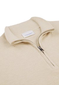 Ljust beige zip-neck tröja gjord av texturerat stickat material. Har en ribbad krage och en silverfärgad dragkedja med en logotypetikett.