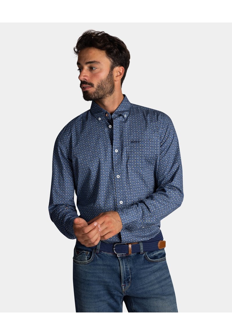 Blauwe overhemd met knopen en een geometrisch patroon, lange mouwen en een puntige kraag. Draagt bij denim en een gestructureerde marineblauwe riem.