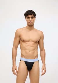 Crne tangice s laganim sivim elastičnim pojasom na kojem se nalazi logo "Calvin Klein". Glatka tekstura i oblikovani dizajn.