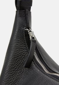 Svart läderhandväska med texturerad yta, silverdragkedjehardware och en elegant design med en slät remdetalj.