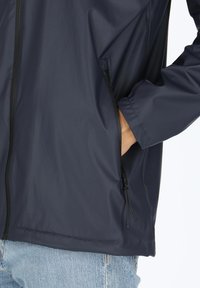 Marineblauw waterdicht jack met een gladde textuur, zwarte ritszakdetail en elastische manchetten. Heeft een minimalistisch ontwerp zonder patronen.