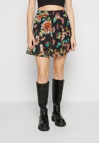 Jupe patineuse fleurie avec un fond noir orné de fleurs orange et vertes, design plissé et taille élastique. Associée à des bottes noires montantes jusqu'aux genoux.