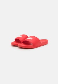 Chanclas de goma roja con una tira ancha que presenta un detalle del logo en blanco, suela plana y textura suave para una comodidad casual.