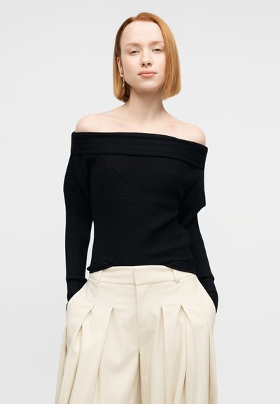 Μαύρο ριγωτό πουλόβερ με αποκαλυπτικούς ώμους και μακριά μανίκια, σε συνδυασμό με κρεμ πλισέ παντελόνι με πλαϊνές τσέπες. Απλός και σύγχρονος σχεδιασμός.