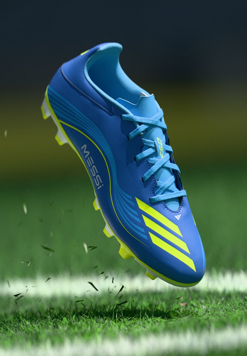 Scarpina da calcio blu con accenti verde, caratterizzata da un design aerodinamico, una parte superiore testurizzata, lacci e tacchetti visibili per la trazione sull'erba.