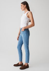 Jeans skinny en denim bleu avec deux poches avant, une fermeture à bouton et un léger délavage. Associés à un débardeur blanc à côtes et des mocassins marron.