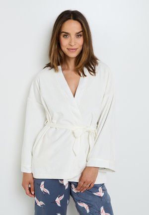 Robe blanche à manches larges et ceinture à nouer ; tissu doux ; associée à un pantalon bleu marine avec un motif d'oiseaux. Texture lisse, design décontracté.