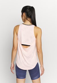 Light pink tank top with a round neckline, back cutout, and subtle "NIKE" pattern. Paired with navy blue shorts featuring textured accents.