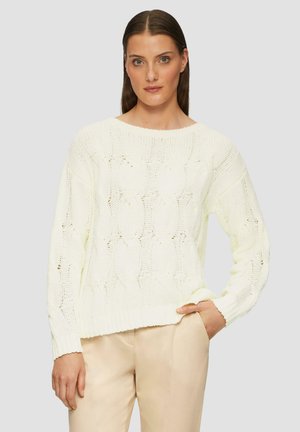 Maglione di maglia chunky giallo chiaro con scollatura a barca, motivo strutturato e maniche lunghe, abbinato a pantaloni beige.