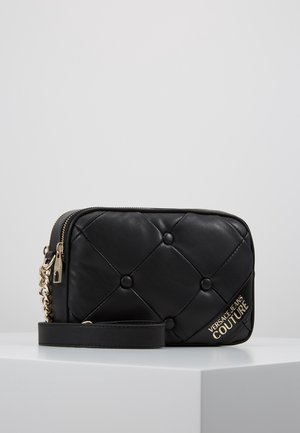 Schwarze gesteppte Leder-Crossbody-Tasche mit goldenem Kettenriemen und „Versace Jeans Couture“-Logo in Gold an der vorderen Ecke.
