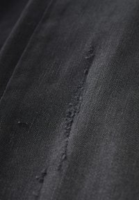 Zwart denim stof met een gestructureerde afwerking, met een zichtbare naad en rafelige randen, die een casual en robuust ontwerp benadrukt.