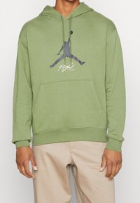 Felpa verde oliva con tasca a marsupio frontale, caratterizzata da un logo Jumpman grigio scuro e la scritta "Flight" stampata sul petto. Tessuto morbido, vestibilità comoda.