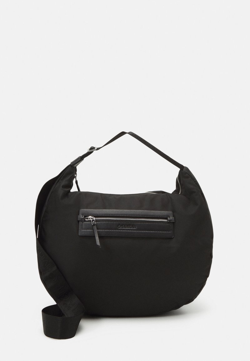 Sac à bandoulière noir en forme de croissant avec sangle réglable et poche zippée à l'avant sur un fond uni.