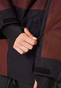 Water-resistant jacket with a maroon and black color-block design. Features an adjustable drawstring and Velcro closure at the cuff.