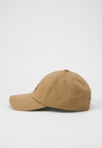 Tan baseball cap with a curved brim, cotton material, feature stitching, and an embroidered design on the front. Side view.
