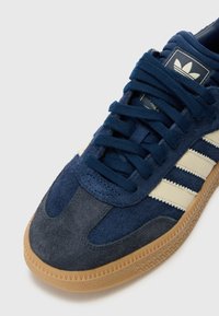 Zapatillas de gamuza marinas con rayas crema, suela de goma y punta redondeada. Presenta un upper texturizado y un cordón tradicional.