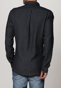 Camicia a maniche lunghe in denim scuro con colletto, dotata di una piega sul retro, polsini abbottonati e un sottile motivo testurizzato.