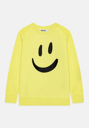 Gul sweatshirt i mjukt tyg med en stor svart smiley-ansikte grafik i mitten. Klassisk rund hals och ribbade ärmslut.
