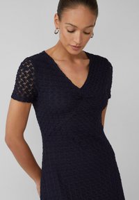 Robe marine de longueur genou avec un motif texturé, à manches courtes et décolleté en V. Présente une silhouette ajustée et une légère extensibilité.