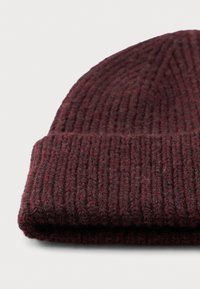 Kurrutatud tume punane kudumisvillane beanie müts, millel on ribikate tekstuur, valgel pinnal.